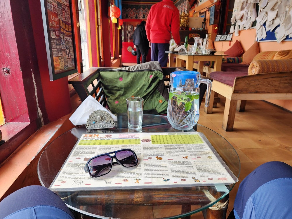 Café table with a menu, sunglasses and a water jug, in a colourfully decorated restaurant