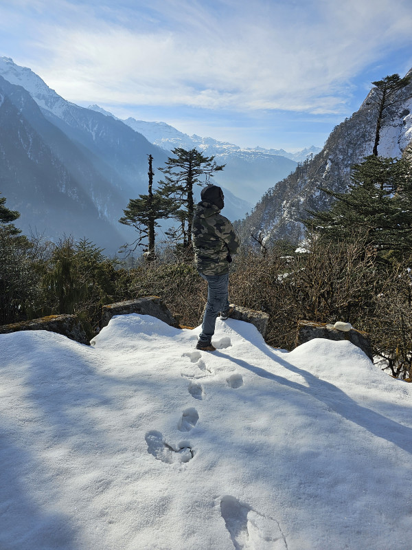 Man standing in snow at a cliff edge, looking over a deep Himalayan valley